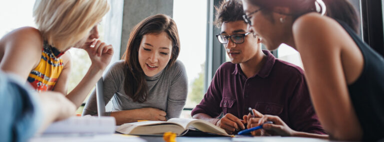 Group of young people sitting at table reading books