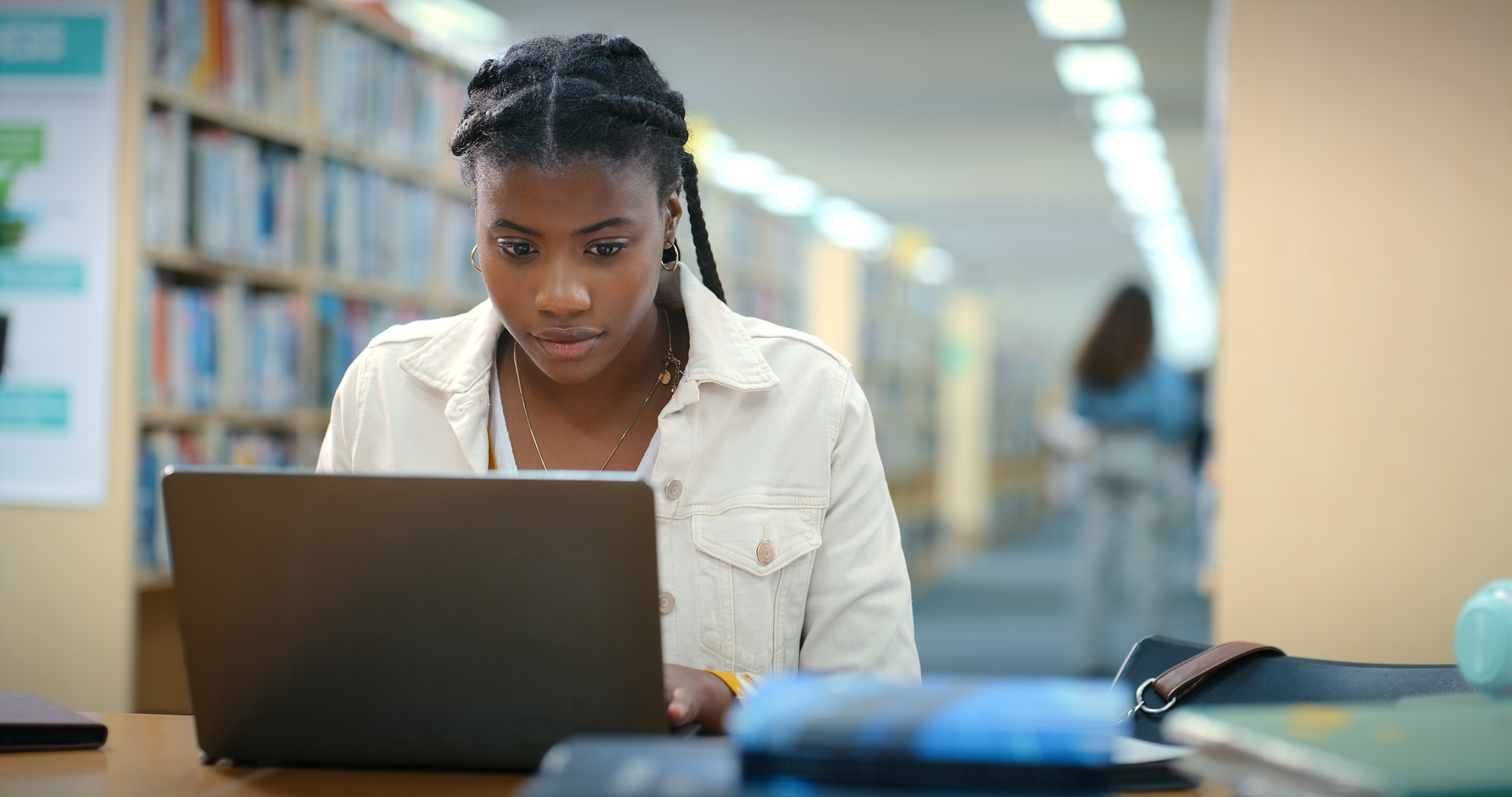 Student types at laptop computer while sitting in library.