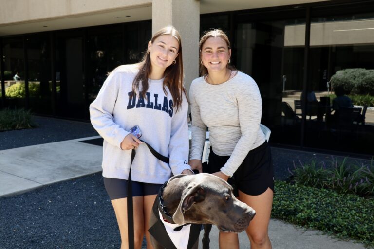Two Parker students smile while posing with Parker, Parker University's security dog (a great dane)